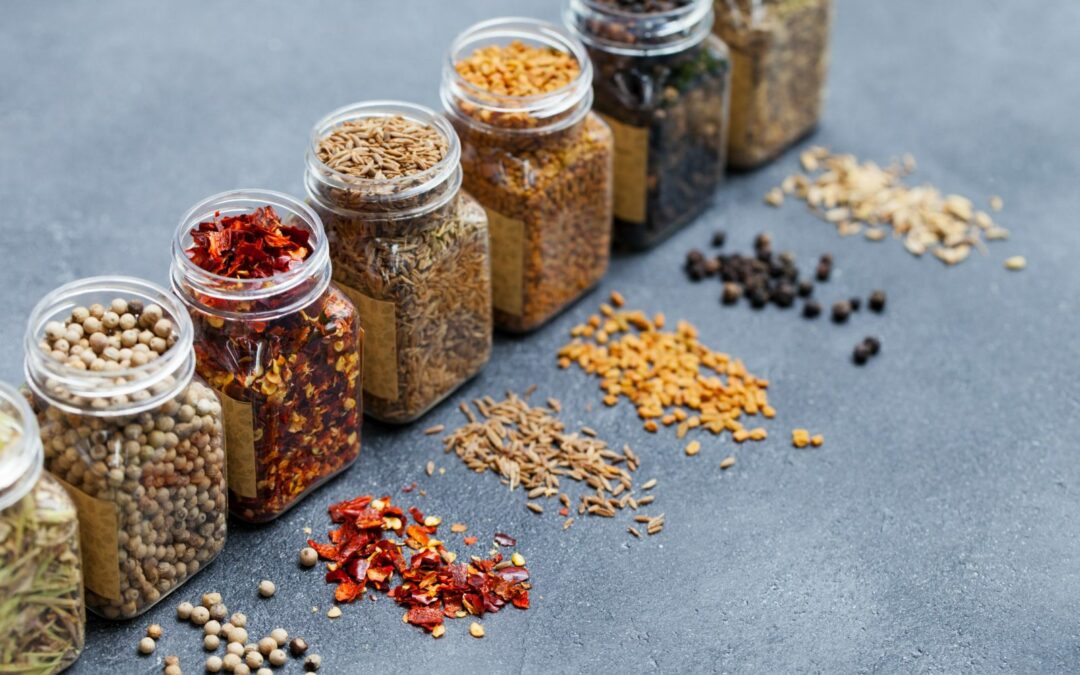 Assortments of spices, white pepper, chili flakes, lemongrass, coriander and cumin seeds in jars on grey stone background. Copy space